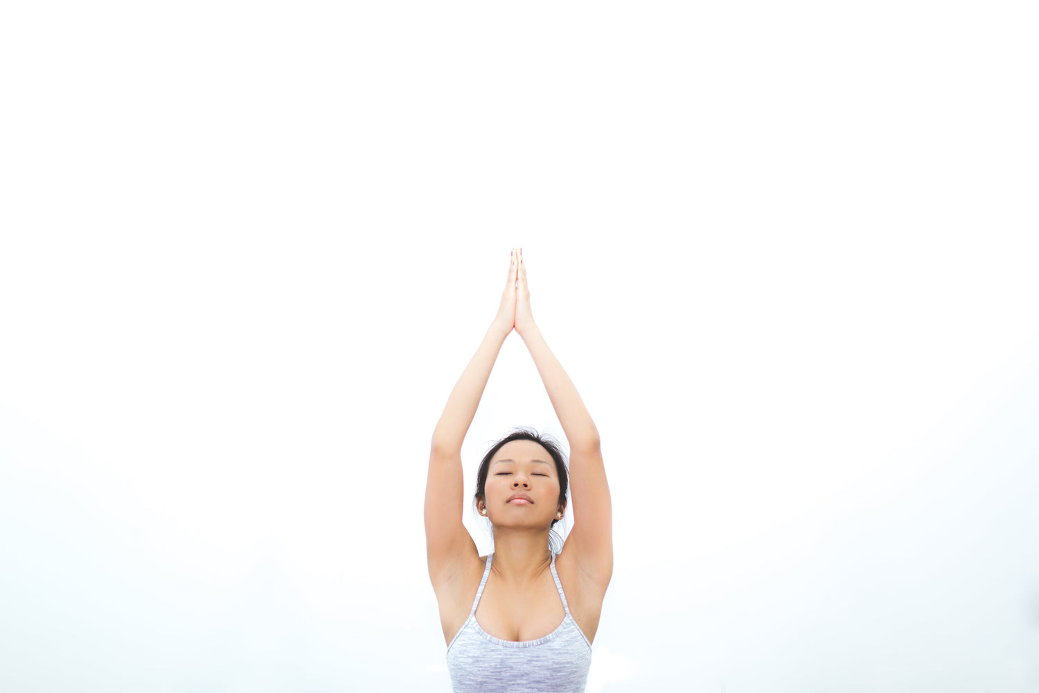 Woman practicing tempo training for strength gains with hands raised in prayer position against a bright background.