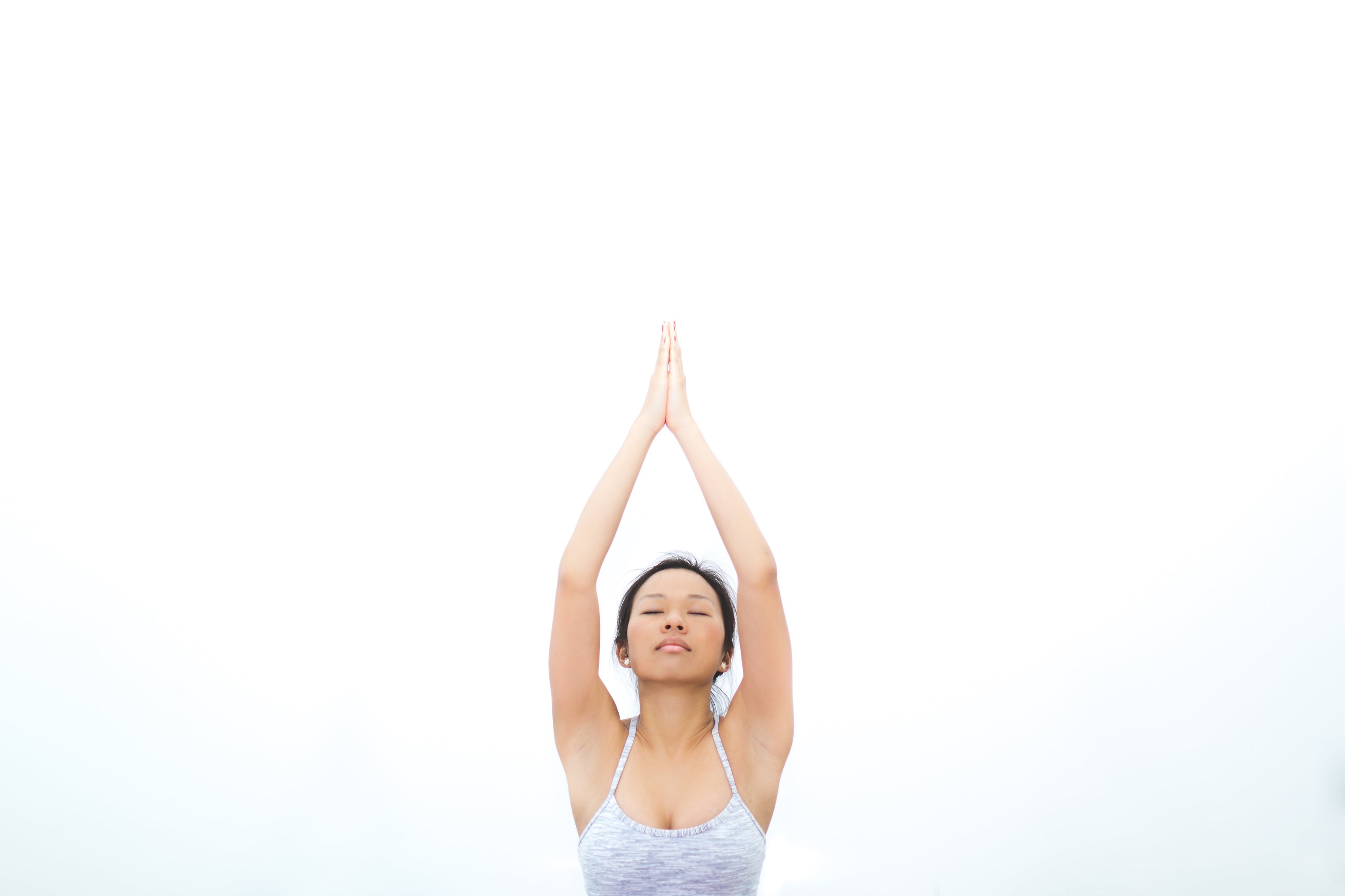 Woman practicing tempo training for strength gains with hands raised in prayer position against a bright background.